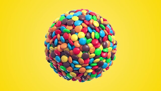 Colorful coated chocolate candies in the shape of a sphere rotate on yellow background. Seamless loop. Alpha layer is included. 3d rendering