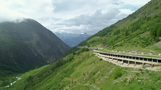 AERIAL Flying along a covered mountain pass in the vibrant green Swiss Alps. Cinematic drone point of view of the Simplon pass in the picturesque mountains of Switzerland. Scenic route across mountain