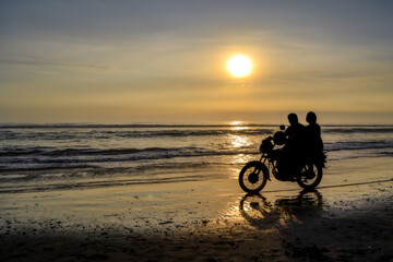 Obraz na płótnie Canvas Silhouette of two people on a motorcycle, in the background a beach at sunset.