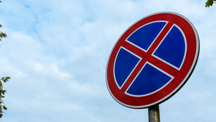 Round road sign with a red cross on a blue background. A sign means a parking prohibition. Dramatic sky background. Space for text.