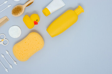 Baby care concept. Evening baby bathing. Flat lay composition of bathing accessories for newborn - hair brush, sponge, rubber duck, cream, shower gel, cotton bud - on grey background. Place for text.