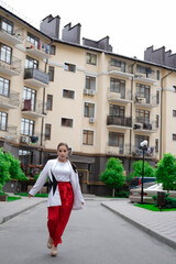 confident brunette woman in red pants and white blouse and jacket walking in the street