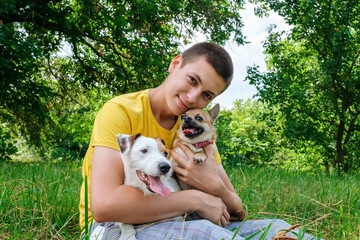 Young caucasian man hugs two dogs Jack Russell and a chihuahua and resting in the summer park