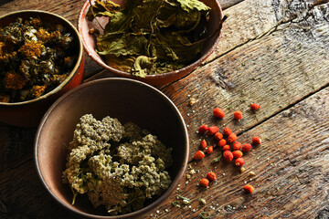 A top view image of rustic country bowls filled with organic herbal medicines of yarrow, plantain, rose hips, and dandelion.