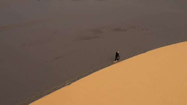 Old man in black is engaged in kung fu in the dunes at sunset. a lot of sand, golden sunset light. sports training. handsome man meditating. Man walks by the side of sand dunes