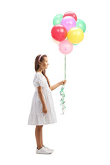 Full length profile shot of a girl in a white dress holding a bunch of balloons