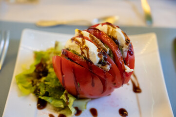 Big red french tomato served with fresh mozzarella cheese, basil pesto and creme balsamico as starter in restaurant in Provence, France