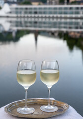 Tasting of white quality riesling wine served on outdoor terrace in Mosel wine region with Mosel river and old German town on background, Germany