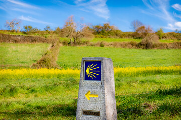 Way Marking Stone Post with Scallop Shell Symbol and Yellow Arrow Sign in the Spring Field outside...