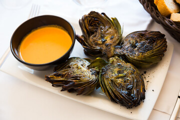 Delicious grilled artichoke halves served with romesco sauce on plate