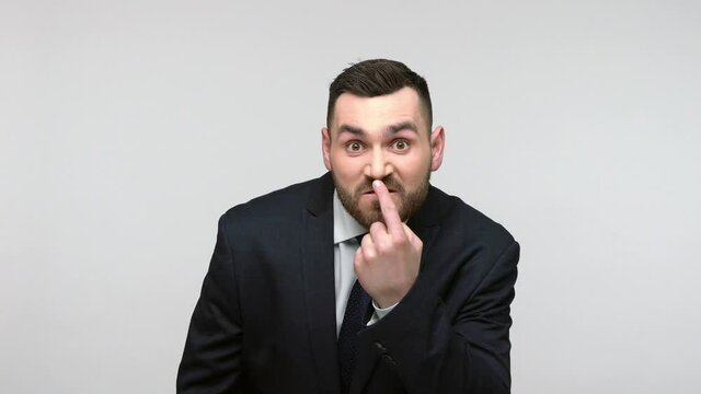 Aggressive bearded businessman in black official style suit pointing at his nose showing lie gesture and looking at camera with anger. Indoor studio shot isolated on gray background.
