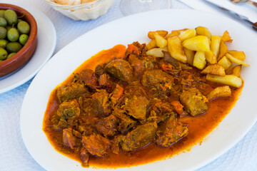 Image of tasty baked pork cheeks in sauce with potatoes on plate, nobody