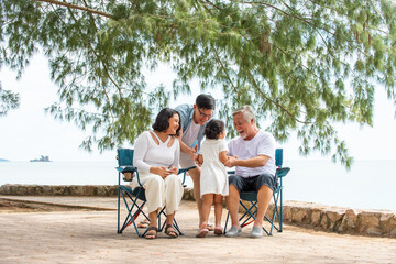 Happy multi generation Asian family enjoy picnic travel together on the beach in summer. Parents with retired senior grandparent and cute child girl relax and having fun on summer holiday vacation