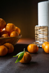 a tangerine in the foreground and more tangerines and oranges in a basket in the background.