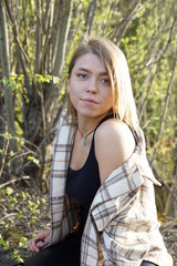 Smiling girl with light brown hair and a checkered shirt, sunny warm day.She enjoys the summer sun and life.