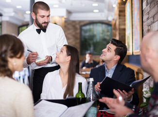 Employee smiling waiter man taking order from positive guests at restaurant