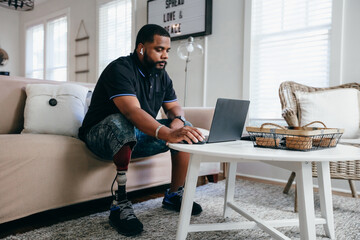 Black man with prosthetic leg working from home on laptop