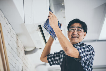 Young Asian male technician wearing safety glasses and apron cleaning air conditioner by removing the filter