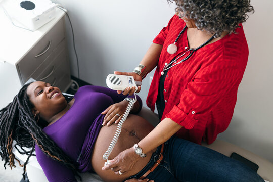 Female doctor uses sonogram doppler to listen to fetal heartbeat, Black pregnant patient 