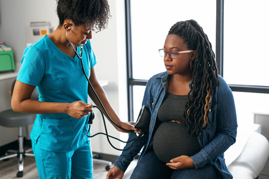 Black woman nurse checks vitals of pregnant patient - Powered by Adobe