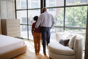 Rear view of father and son standing in front of window in living room