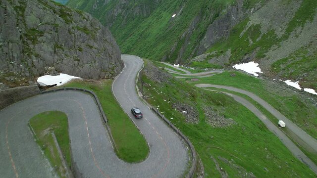 DRONE: Grey colored tourist car cruises along the scenic switchback road of Passo San Gottardo. Tourists on road trip across the mountains of Switzerland drive along hairpin turns of Gotthardpass.