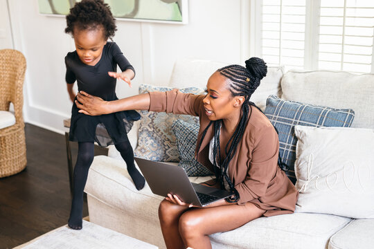Black daughter interrupts mom working from home on laptop