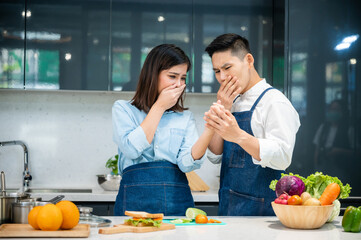 Young Asian woman crying in pain due to a knife cut in finger while chopping vegetables in kitchen...