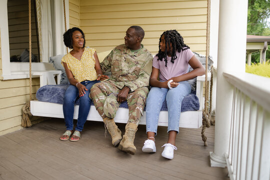 Military dad talks with wife and daughter on front porch swing, African American