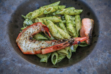 Closeup Penne Pasta with Pesto Sauce and prawn on plate on black table. Vegetarian healthy Italian food.