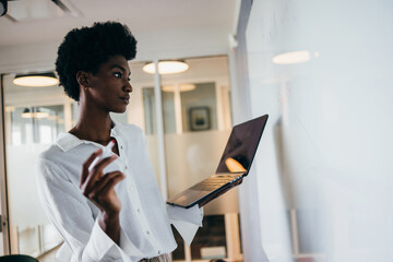 Focused Black businesswoman with laptop brainstorming on whiteboard