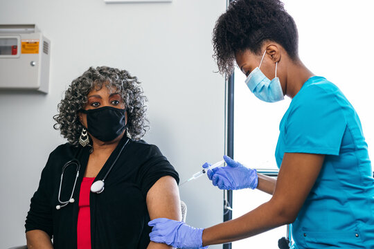 Senior female doctor gets vaccine, from black nurse