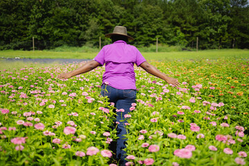 Rear view of woman in purple shirt and hat walking in field of pink flowers, African American