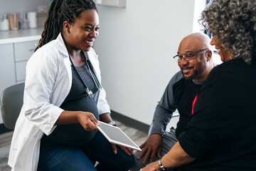 Black pregnant doctor explains lab results to senior patients using digital tablet 