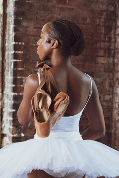 Portrait of attractive Black woman, ballerina dancer wearing tutu and holding pointe shoes