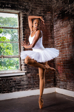 Black ballerina doing powerful ballet dance pose, wearing pointe shoes and white tutu
