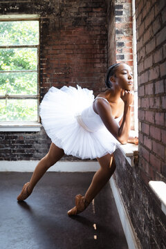 Black ballerina doing powerful ballet dance pose, wearing pointe shoes and white tutu