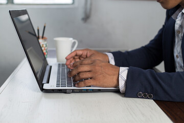 Side view of unrecognizable businessman typing on laptop. Closeup hands on the computer keyboard typing. 