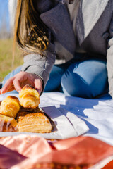 Obraz na płótnie Canvas argentinian facturas, typical argentinian pastry dessert, breakfast of croissants, medialuna at a picnic in a park. Hand of a woman interacting. vertical photo