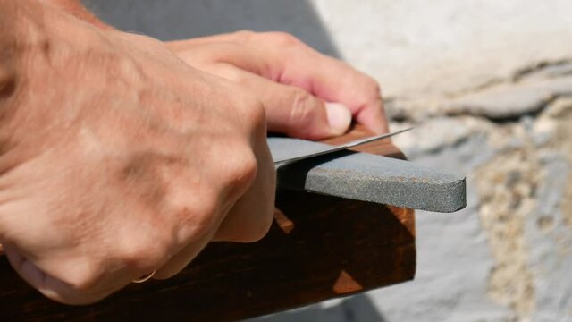 Beautiful man's hands sharpen a knife with a whetstone close-up