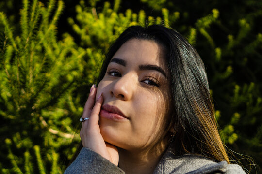 portrait of a young hispanic latin woman looking at camera, green background of plants