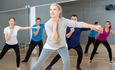 Fototapeta na wymiar Portrait of emotional middle-aged woman doing exercises during group class in dance center