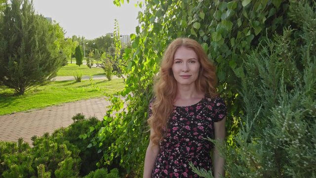Close-up portrait of young lady with long red hair and freckles posing happy state of mind looking at camera in park in summer. Nature mother concept.