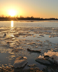 Ice drift on the river against the background of the golden sunset sky, reflected in the cold water. Spring landscape on the river.. Composition of nature.