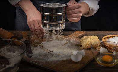 Women's hands, flour and dough. A woman in an apron cooking dough for homemade baking, a rustic home cozy atmosphere, a dark background with unusual lighting.