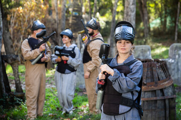 Portrait of young woman paintball player with marker gun ready for game outdoors