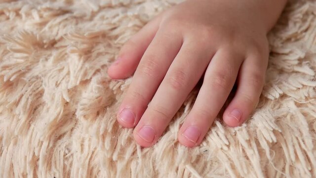 Close-up of a sleeping child's hand moving the fingers on a fleecy blanket