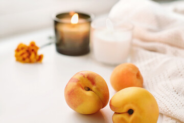fresh ripe peaches, candles and flower next to warm knitted plaid. autumn cozy home concept.fall mood