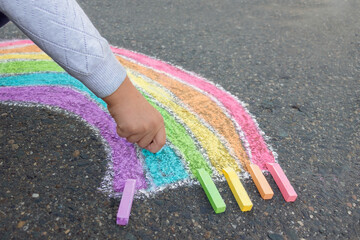 Child draws
 rainbow on the asphalt with colored chalk, outdoors. Side view.