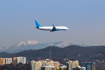 Passenger aircraft flies low over the city against the background of high snow-capped mountains